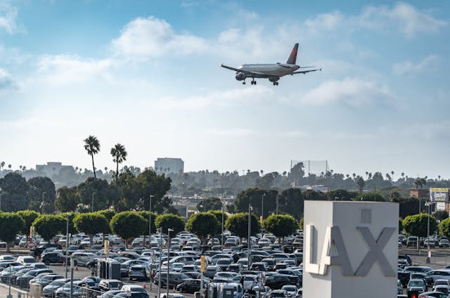 Busy parking lost at Los Angeles International Airport with travelers and traffic and a plane landing
