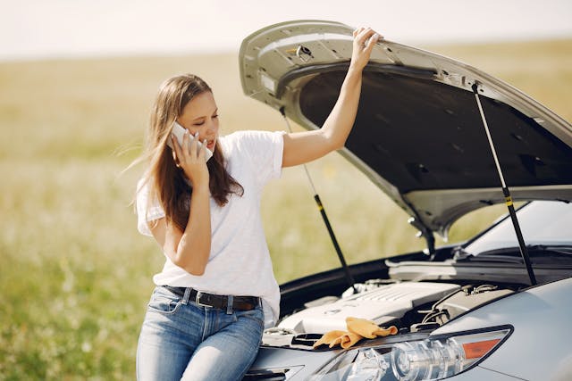woman on phone with insurance under hood of broken down car